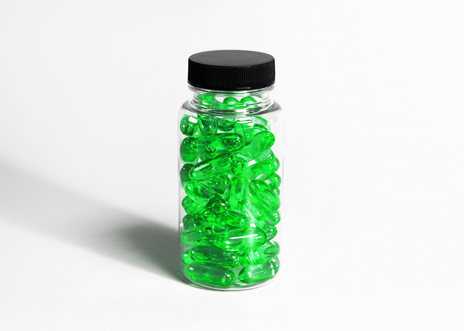 Close-up of transparent bottle filled with green softgel capsules on a white background.