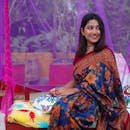 Young woman wearing a colorful floral saree, sitting outdoors with a joyful smile.
